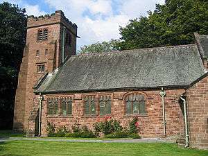 A church see from the south with a castellated tower at the left, roses and a grassed area in the foreground and trees to the left and beyond