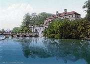 A castle, nestled in trees, beyond a moat, with a bridge.