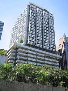 Box-like building with rectangular cross section.  The lower floors are a visible parking garage, while the upper floors have a grey and white facade with protruding windows and a rooftop terrace.