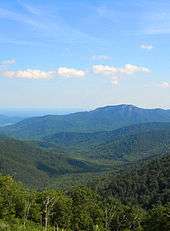 Green tree covered mountains turn blue as the progress toward the horizon.