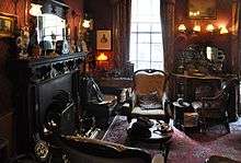 Cluttered room with fireplace, three armchairs and a violin