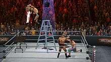 A shirtless masked wrestler attempts to slam a wrestler wearing blue and white striped shorts through two stacked tables, another wrestler wearing jean shorts and sneakers punches a fourth wrestler who is holding his head. All four are in a wrestling ring with a ladder at the center and a briefcase hanging above the ladder, in front of a crowd.