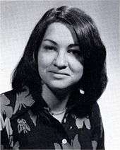 A formal pose of a young woman in her early twenties, dark straight hair parted near the center, wearing a dark floral print top.