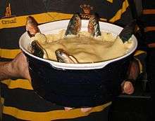 A blue ceramic dish containing a stargazy pie, with six fish poking out of a shortcrust pastry lid, looking skywards