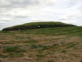 a grassy knoll, the top of which is surrounded by a stone retaining wall