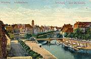 A tree-lined urban river, with a quayside to the centre-left