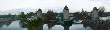 Panoramic image from the river, with three towers at the ends and middle of a stone bridge