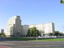 Distant photo of large white multi-story building, with trees in front