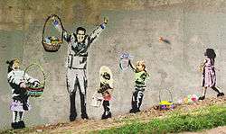 "Easter AIGs" Stenciled mural on a concrete wall depicting four children with empty baskets who are searching for Easter eggs while a man in a suit with a full basket gloats. One of the children has just thrown an egg at the man.