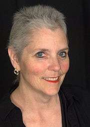 Head shot of Susan smiling with a black background.