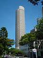 Ground-level view of a 50-storey cylindrical tower with black windows and a small cut-out near the roofline