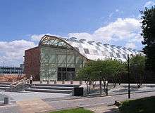 A modern, glass and steel building with a curved roof and steps leading up to it