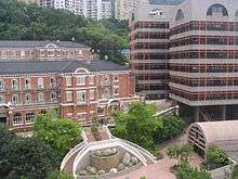 3-storey red brick building with gabled roof adjacent to 7-storey modern building with flat roof.