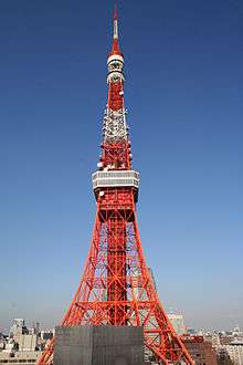 Mid-level view of an orange and white lattice frame; the structure curves and widens near the bottom and comes to a point at the top