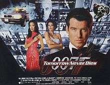 A man wearing evening dress holds a gun. On his sides are a white woman in a white dress and an Asian woman in a red, sparkling dress holding a gun. On the background are monitors with scenes of the film, with two at the top showing a man wearing glasses holding a baton. On the bottom of the screen are two images of the 007 logo under the title "Tomorrow Never Dies" and the film credits.