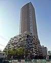 Ground-level view of a rectangular, brown high-rise; it sits on a larger base that has multi-colored panels