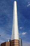 Ground-level view of a tall, white, angular chimney rising from a brown, striped building