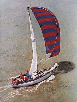 A single-masted yacht under sail, with crew on deck and waving.