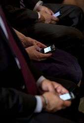 three people in dark suits thumbtyping on BlackBerry's while seated