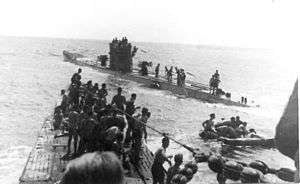 Three-quarter front view over the bow from the conning tower of another submarine with numerous people standing on both vessels