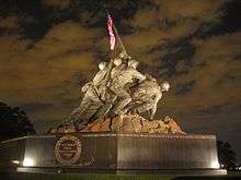 Color photo of the USMC War Memorial, a bronze statue of six men planting a flagpole with an American Flag into the ground.