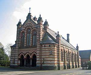 A chapel with rows of red and white bricks; the entrance porch has three arches and there are three windows above