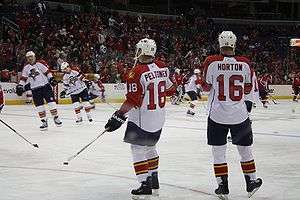 Canadian male in white uniform and white helmet standing next to European male also in white uniform and helmet