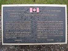 A bronze looking plaque with a small maple leaf in the top centre with English text on the right and French on the left.