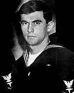 A picture of a man in a United States Navy uniform while looking at the camera with a stern face.