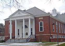 A brick building whose front section has a white triangular roof supported by columns. The inscription on the front reads "Bendheim West Greenwich Civic Center".