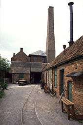 Several red brick buildings and a chimney, with parallel rail tracks in the foreground