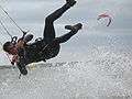  Kitesurfer wearing one-piece wetsuit, hanging from harness, separated from board. 