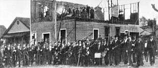 A photograph showing group of rioters posing outside the ruins of the "Record" building