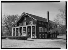 A 3 and a half story building sided with wooden shingles. There is a porch with white pillars at the front of the building.