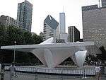 A white outdoor sculpture is fenced off from the public with a backdrop of tall buildings