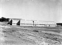 Black and white photograph of large building in the middle of an open grassed area