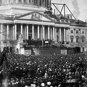 A large crowd in front of a large building with many pillars.