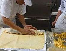 A man shapes the filling on one end of a square of thin dough