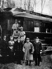 black and white photograph of five men in military uniforms standing side-to-m right, seen outside his railway carriage  in the forest of Compiègne.