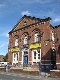 A Victorian brick building with signs on the front in English and Punjabi. The frieze reads "UNITED METHODIST FREE CHURCH 1877", while the sign by the door reads "SRI GURU NANAK SIKH TEMPLE".