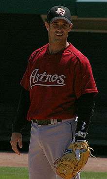 A baseball player standing at first base with his glove, wearing a red jersey with the word "Astros" in front