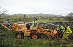 Workers install cables in a trench in a field.