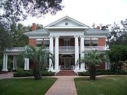  an old southern neoclassical-styled mansion with manicured lawn and palm trees