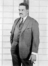 Black and white photo of a white man with a mustache, wearing a suit.