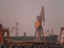 An unfinished ship and an orange crane at the center of an industrial setting