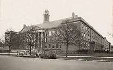 Three-story brick building façade with three white columns surrounding a brown wooden door located on the ground floor