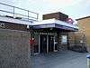 A squat bricked building behind a concrete wall with a dark blue sign reading "BROMLEY-BY-BOW STATION" in white letters