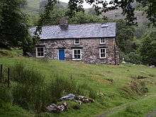 A colour photograph of a stone cottage on a hill