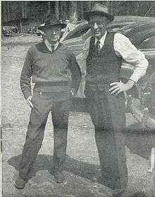 Black and white photo of two men standing outdoors in a forested area