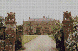 Yellow stone building at the end of a driveway accessed via stone gateposts.